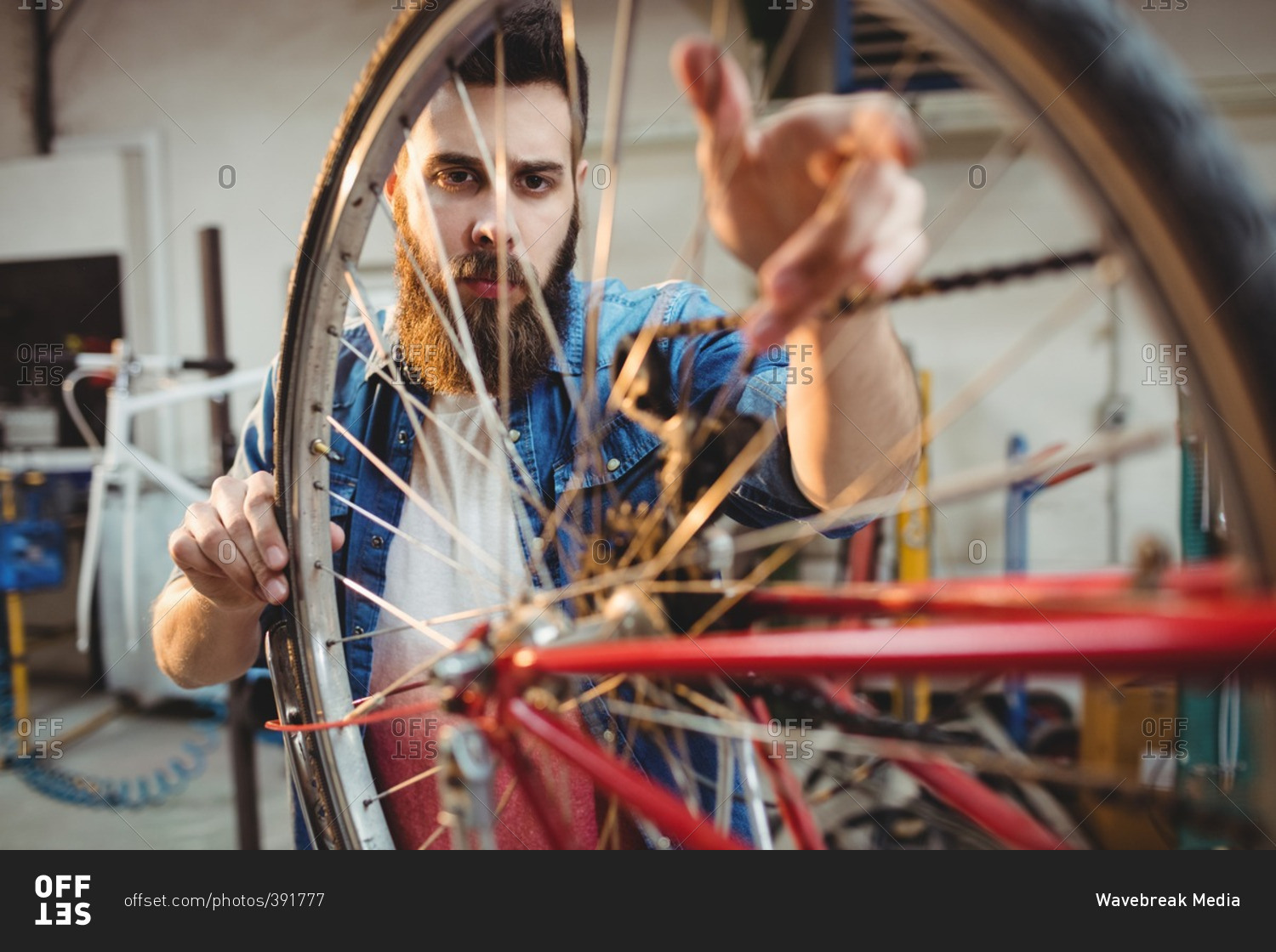 Portrait of a hipster repairing a bicycle wheel in a workshop