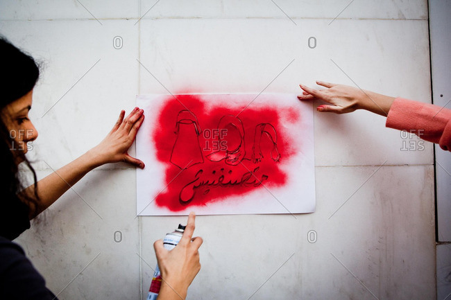 Egypt - March 8, 2013: Girls spray painting stencil onto a wall