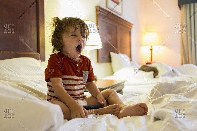 Boy sitting in hotel bed with smartphone yawning
