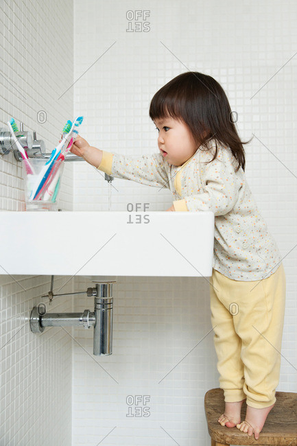 Girl toddler on tiptoe reaching over bathroom sink