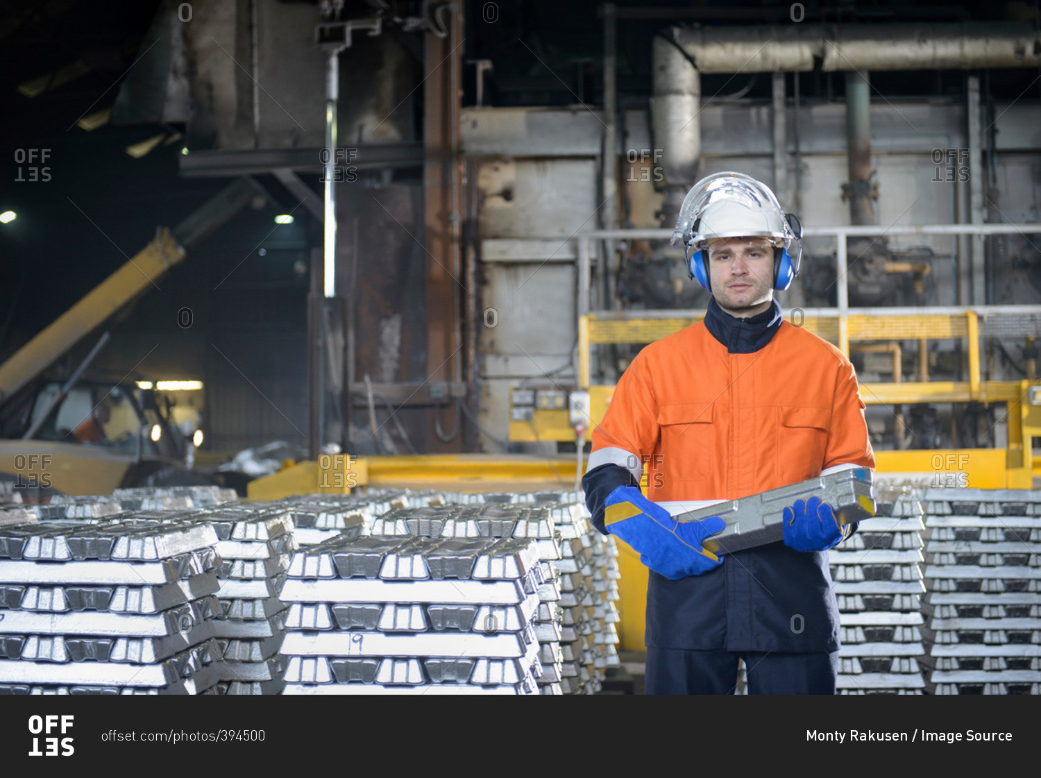 Worker in protective work wear carrying aluminum ingot in foundry