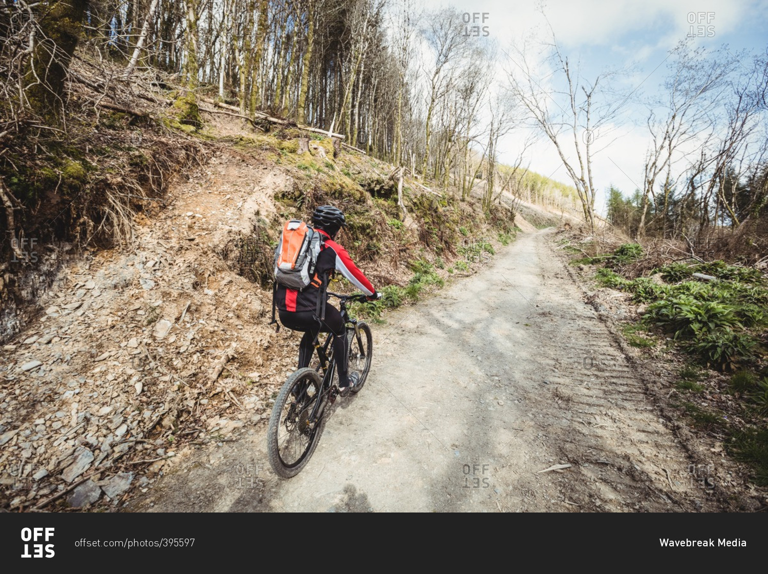 Rear view of mountain biker riding on dirt road on mountain