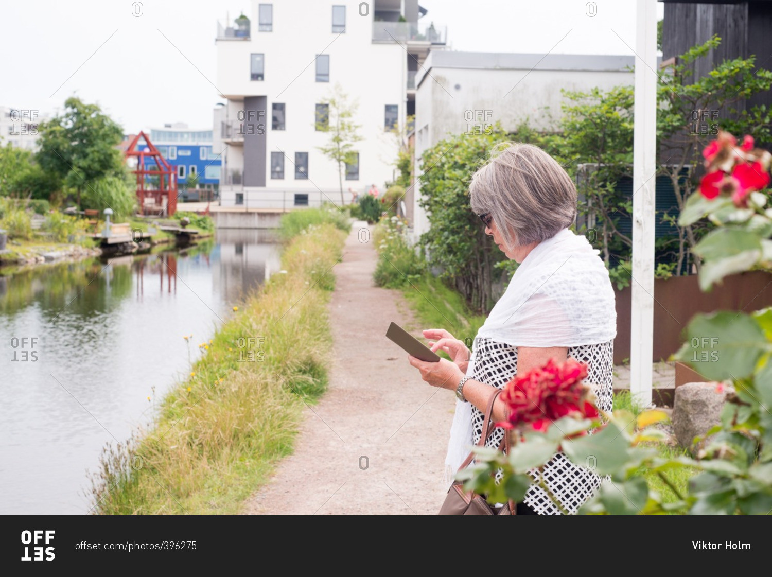 Older woman standing by a river while texting on her cell phone