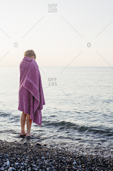 Sweden, Gotland, Lickershamn, Boy wrapped in towel standing at seashore at sunset