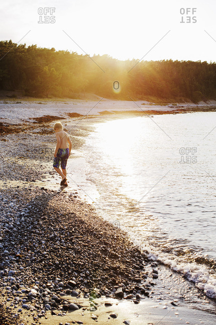 Sweden, Gotland, Lickershamn, Boy walking on beach at sunset