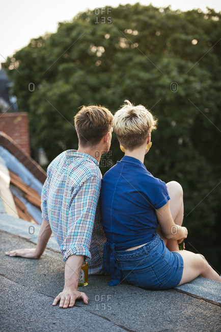 Germany, Berlin, Young couple sitting on rooftop with beer