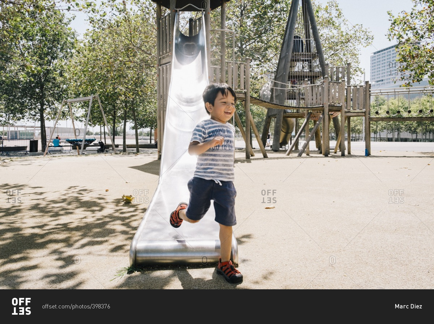 Boy running and laughing in front of a slide on a playground