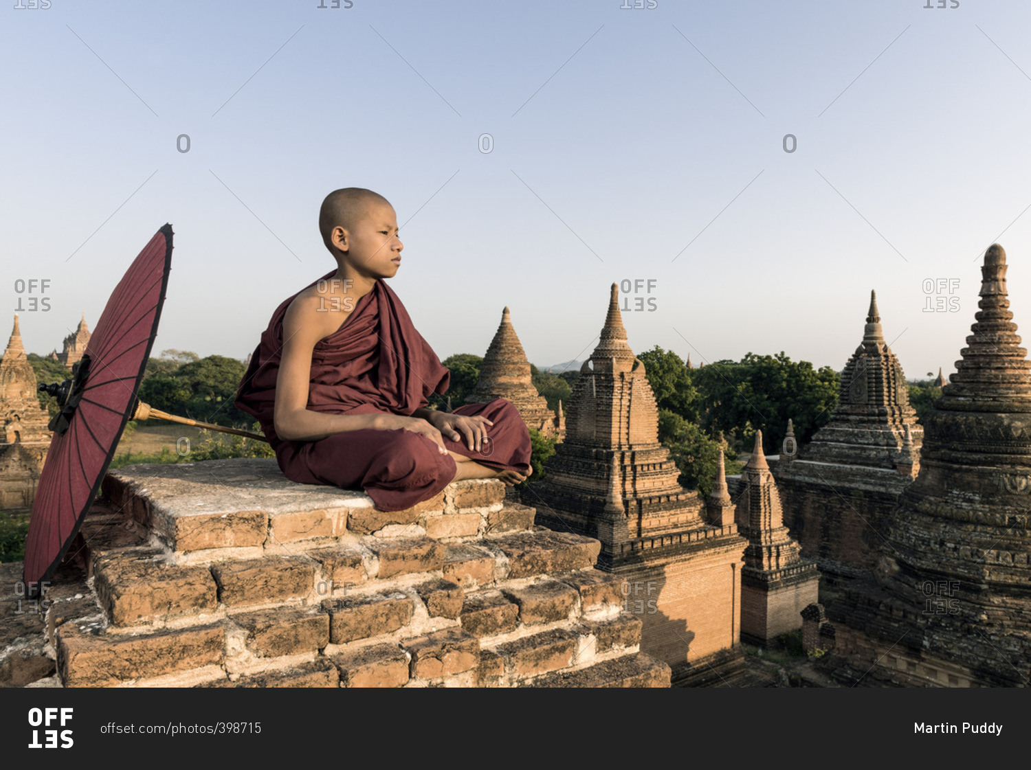 Young Buddhist monk overlooking ancient temples while holding traditional parasol
