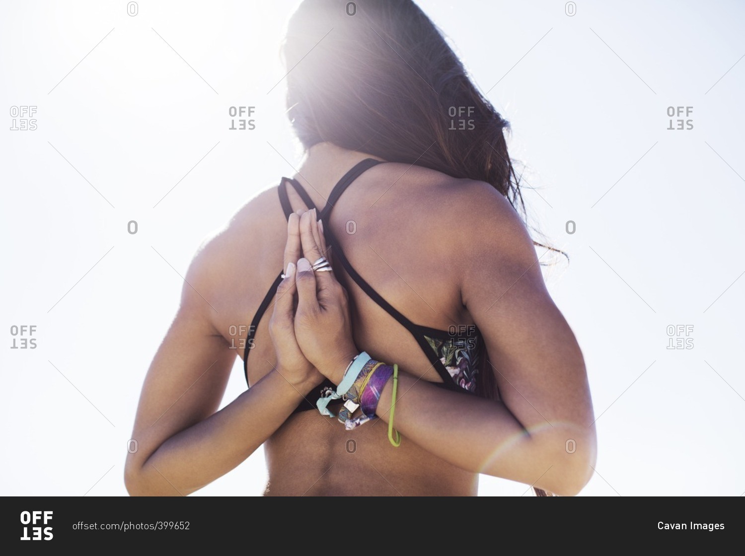 Rear view of young woman doing reverse prayer pose against clear sky on sunny day