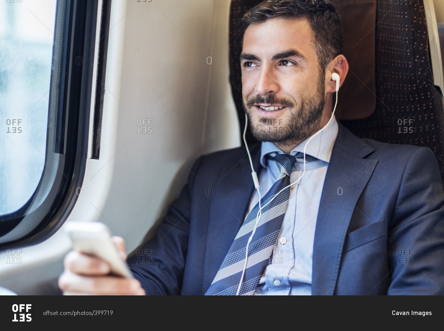 Smiling businessman listening music through smart phone in train