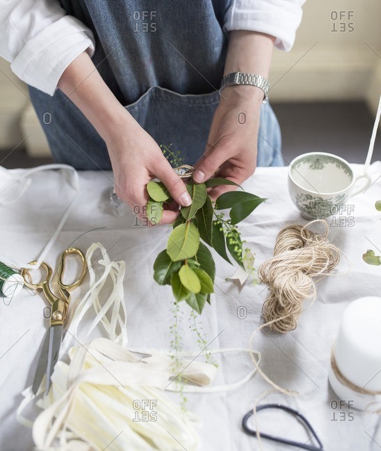 Midsection of woman holding leaves for decorating candle in creative workshop
