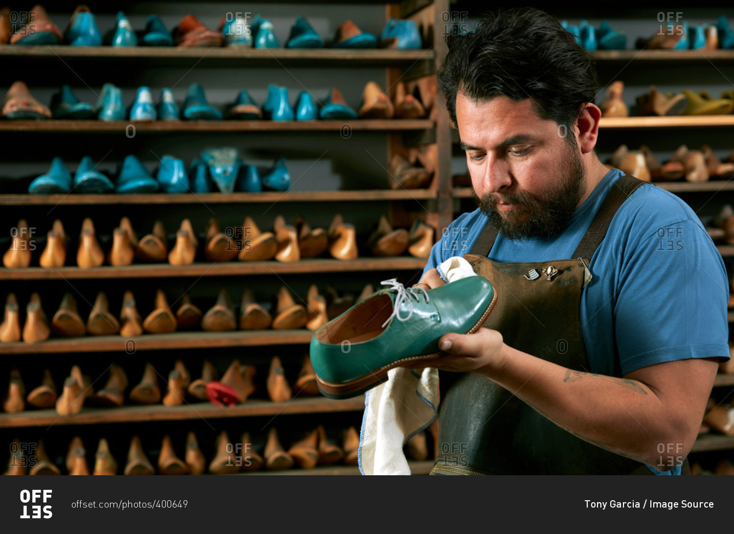 Male cobbler in traditional shoe shop polishing green brogue