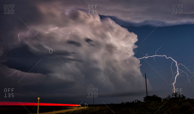 Vehicle light trails and lightning bolt arcing laterally from storm cloud