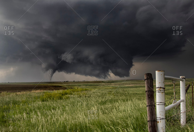 A large cone tornado touches down in an open country field from a very large angled ground-scraping wall cloud