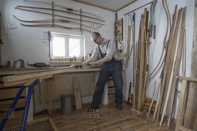 Male bow maker shaving wood and giving it a shape of bow in workshop, Bavaria, Germany