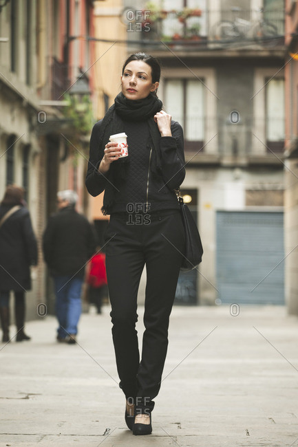 Spain- Catalunya- Barcelona- young black dressed businesswoman with coffee to go in front of a street