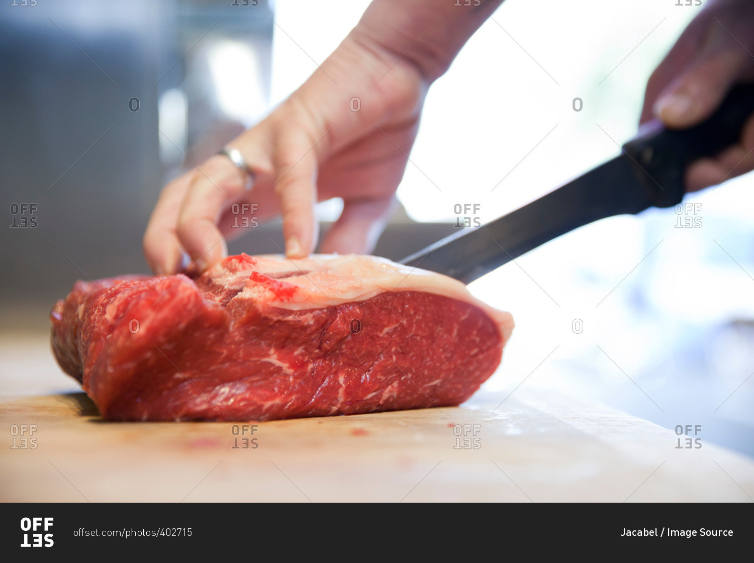 Close up of butchers hands slicing raw steak on butchers block