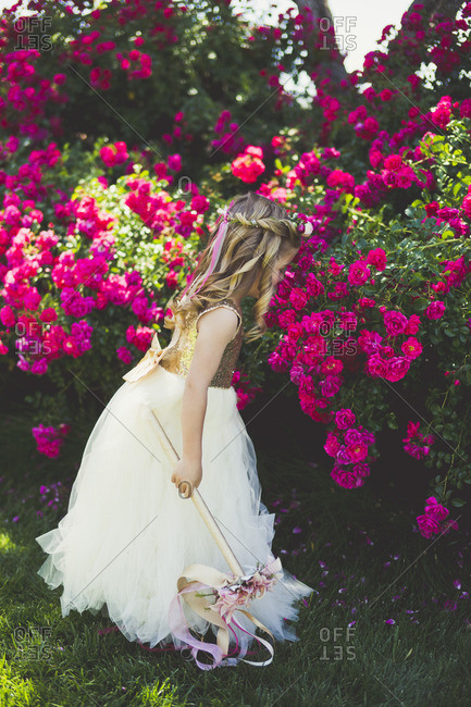 Girl dressed like a princess smelling flowers in a garden stock photo -  OFFSET