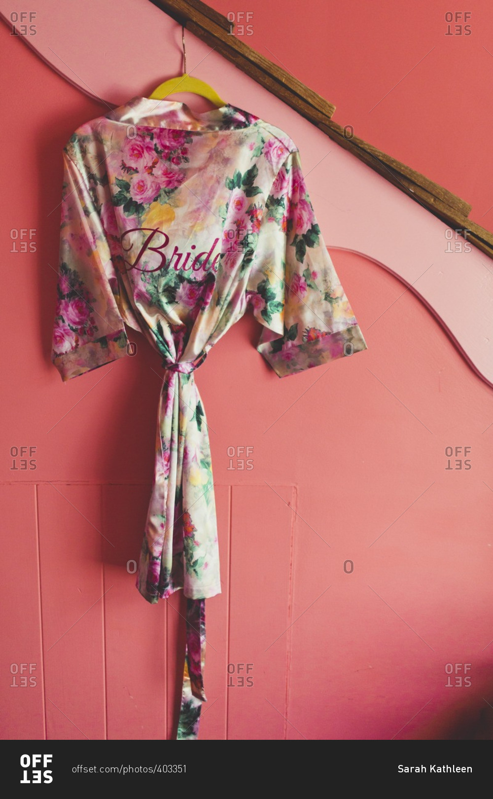 Satin floral robe embroidered with the word 'bride' hanging on a pink wall