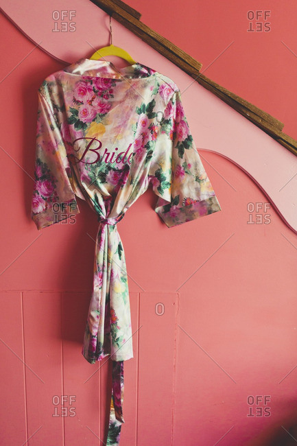 Satin floral robe embroidered with the word 'bride' hanging on a pink wall