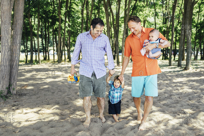 Homosexual couple walking with sons on beach