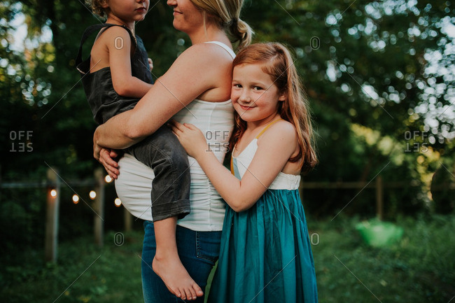 Little girl hugging her pregnant mother who is holding little boy
