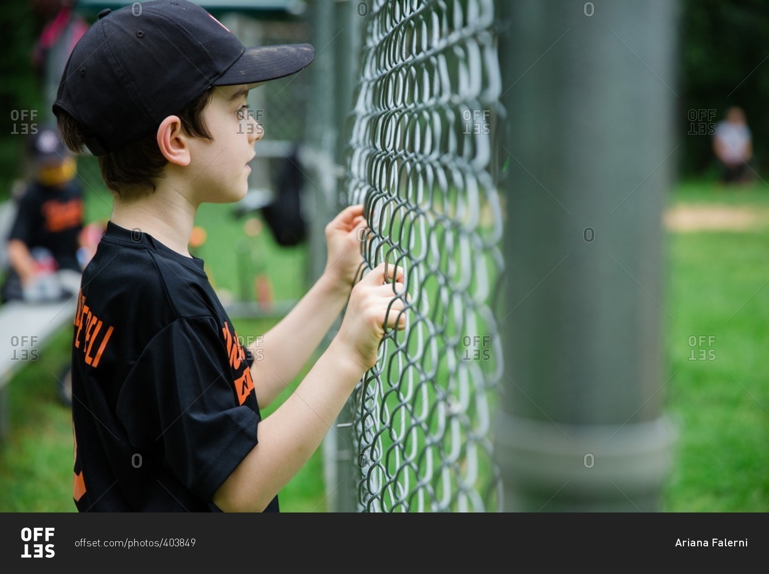 Boy holding onto chain-link fence watching baseball game