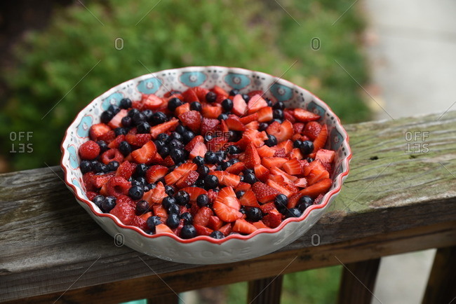 Bowl of mixed berries sitting on a wood railing