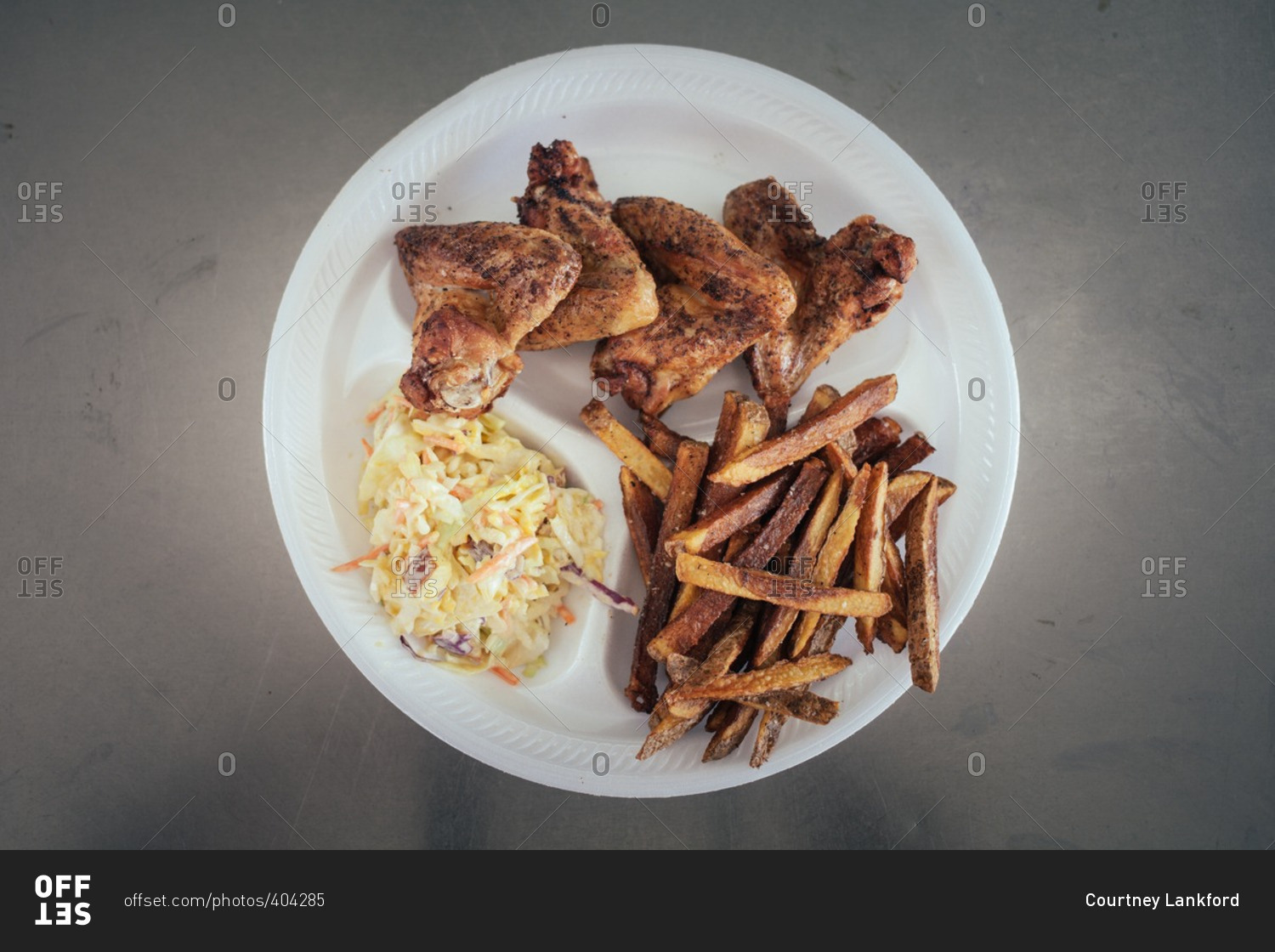 Chicken wings, fries and coleslaw on a disposable plate