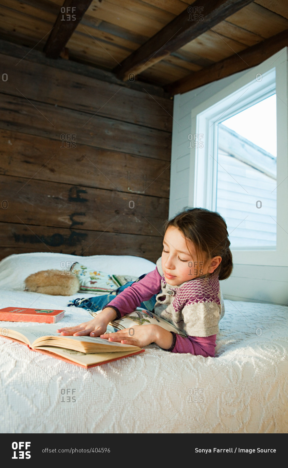 Young girl lying on bed reading book stock photo - OFFSET