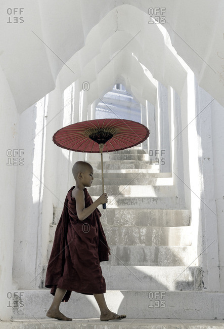 Young Buddhist monk walking through a temple holding a parasol