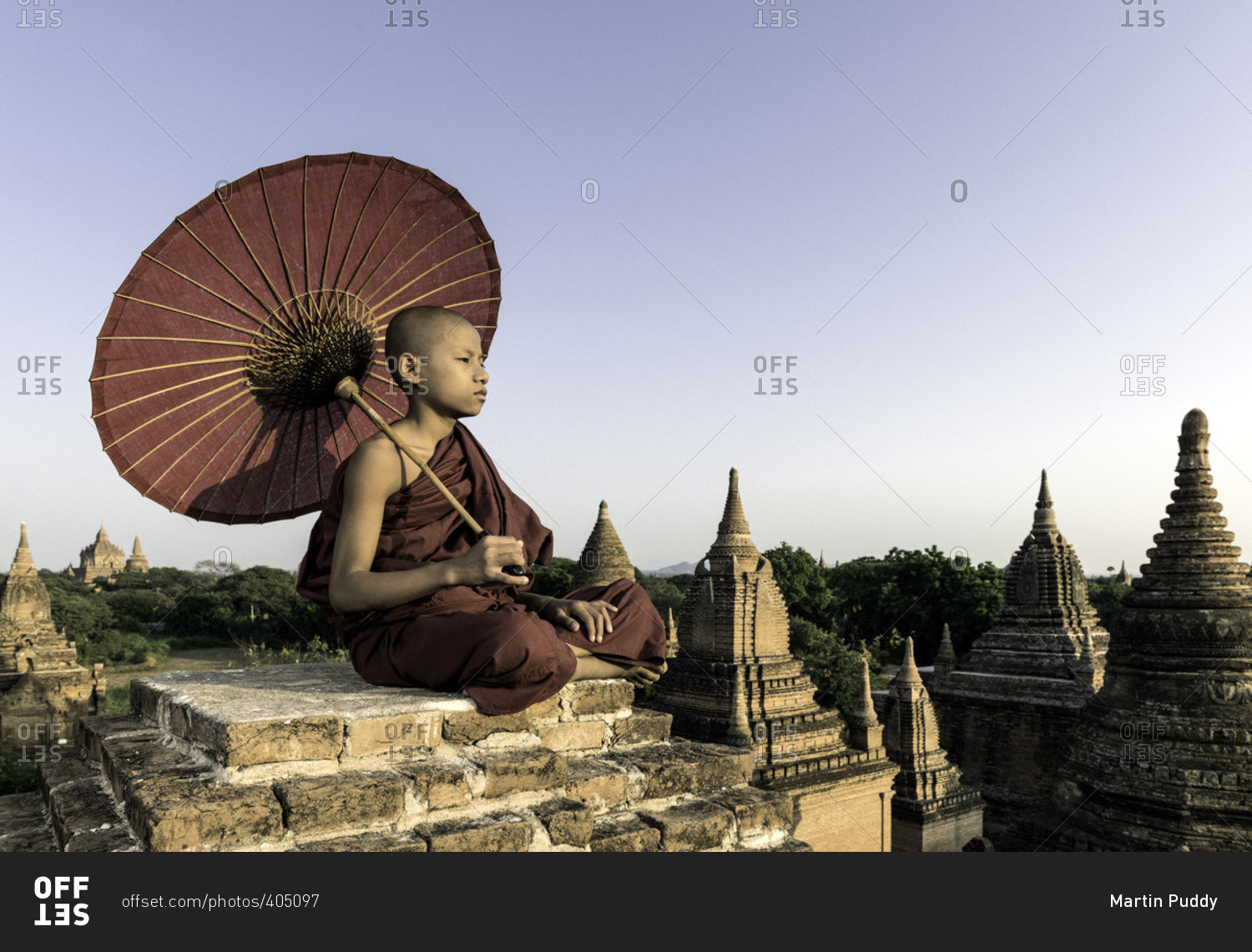 Young Buddhist monk sitting on a temple top holding a parasol
