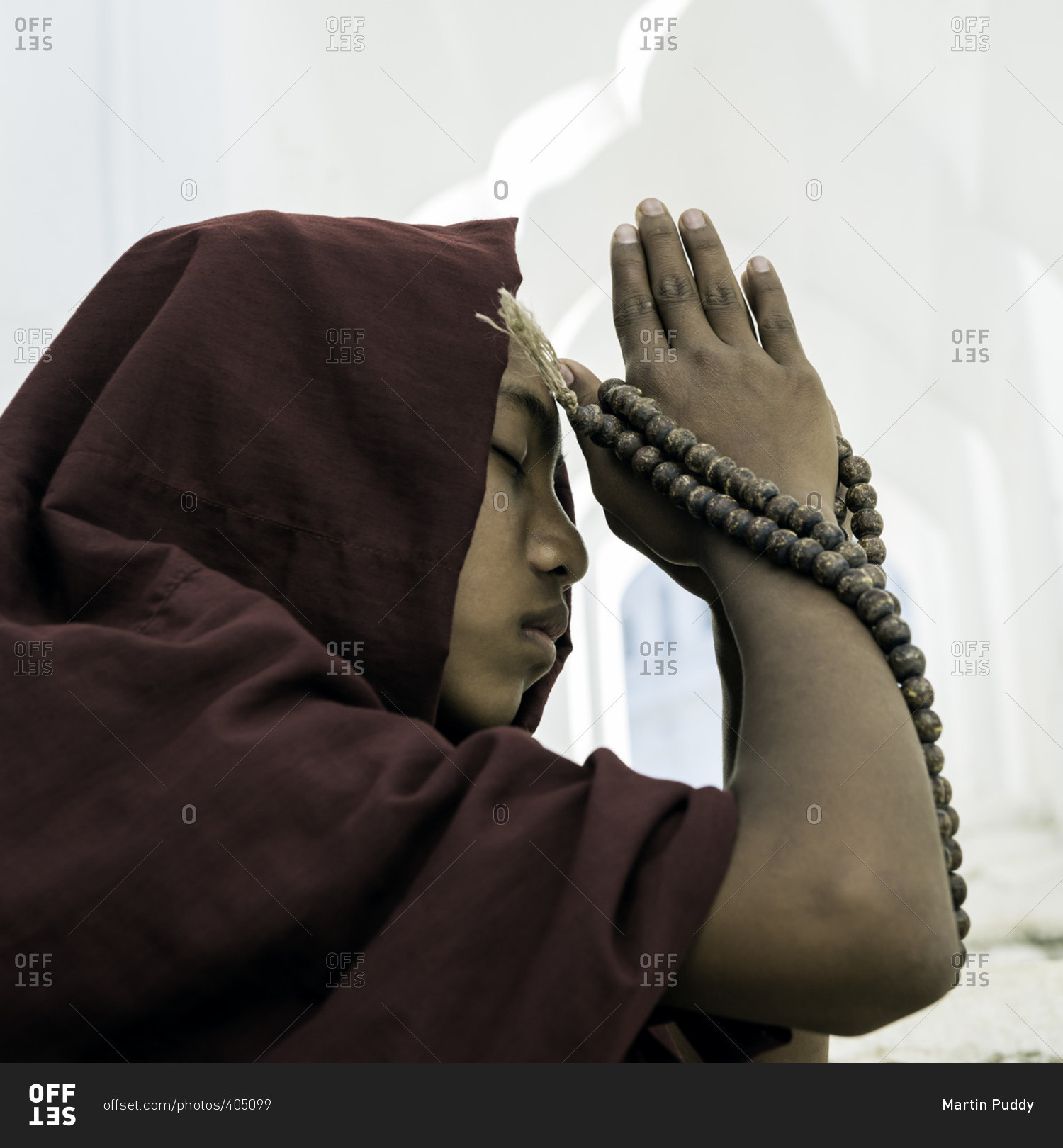 Young novice Buddhist monk praying inside temple corridor, with prayer beads