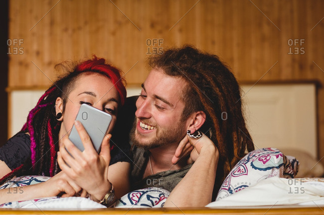 Young hipster couple using mobile phone on bed at home