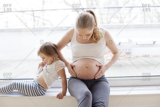 Pregnant mother touching tummy with daughter sitting next to her