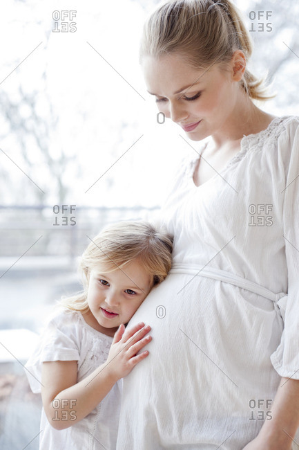 Young girl with head against pregnant mother's tummy