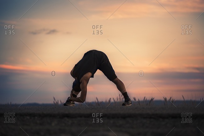 Athletic man stretching in front of colorful sunset