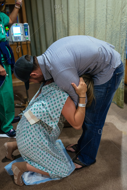 Pregnant woman on her knees holding her husband in a hospital room during pre-labor