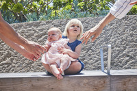 Adults reaching towards two small children on a bench