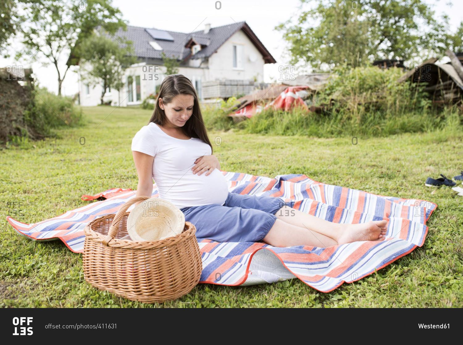 Pregnant woman sitting on picnic blanket touching her belly