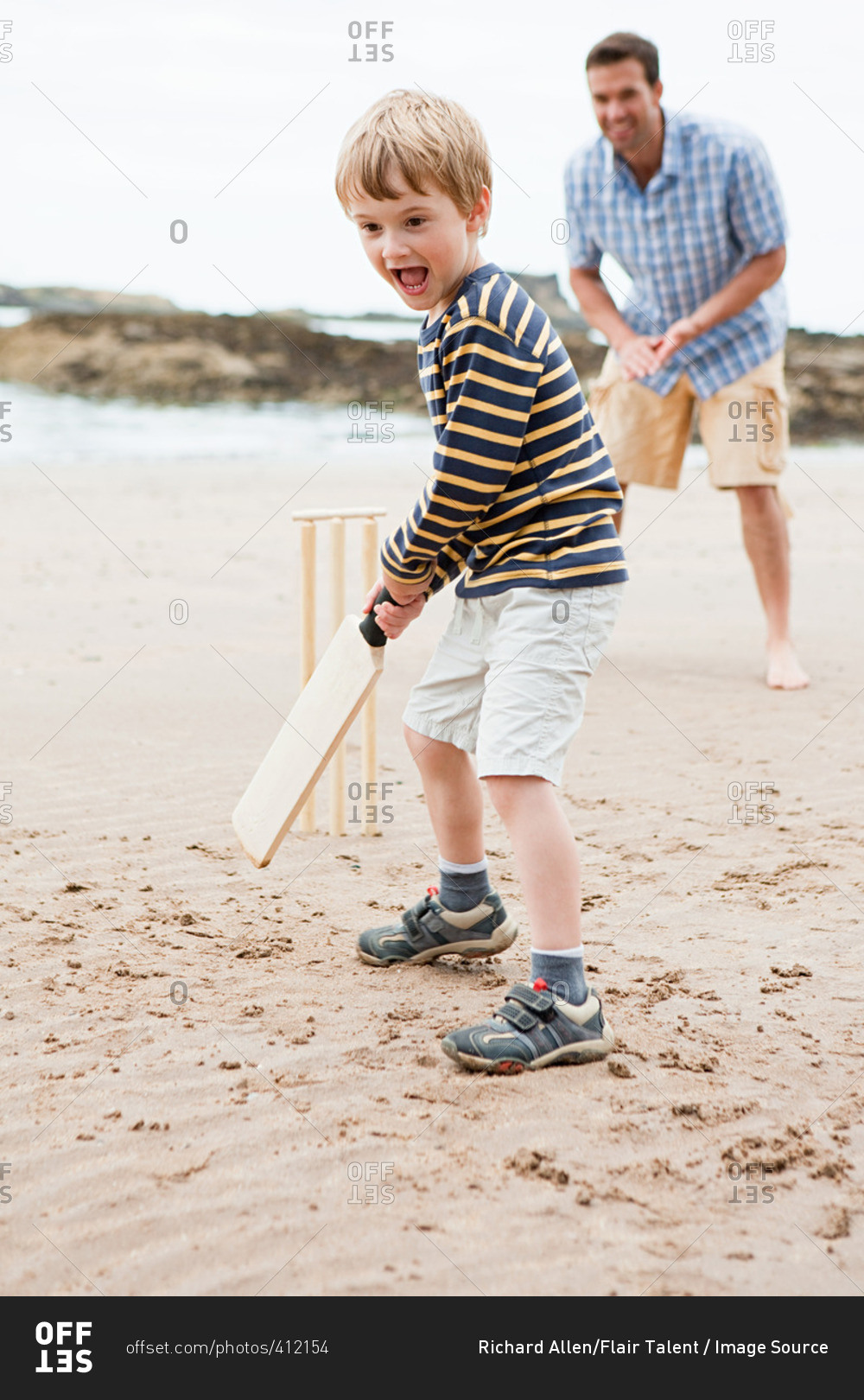 Father and son playing cricket on beach