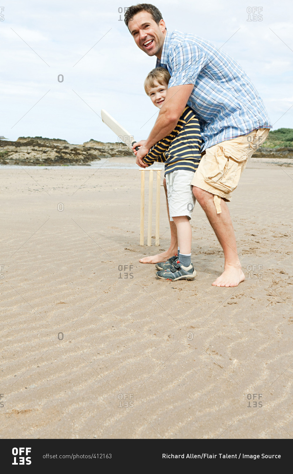 Father and son playing cricket on beach