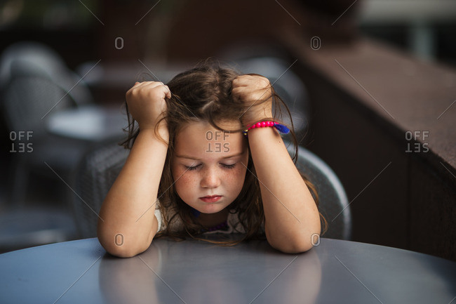 Frustrated young girl with eyes closed gripping her hair at table