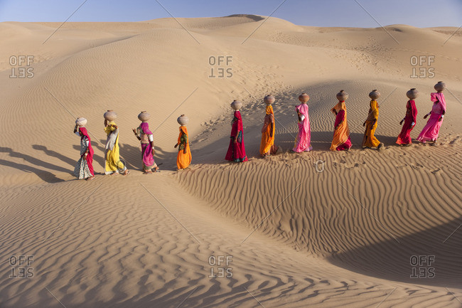 Women bear the responsibility of fetching water from the sparse wells within Rajasthan's vast Thar Desert. Trekking up the side of a sand dune, women expertly balance large clay water vessels atop their heads. Rajasthan, India