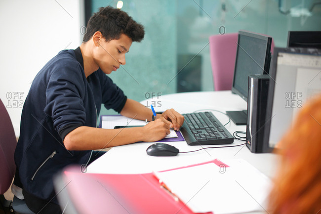 Young male college student at computer desk making notes