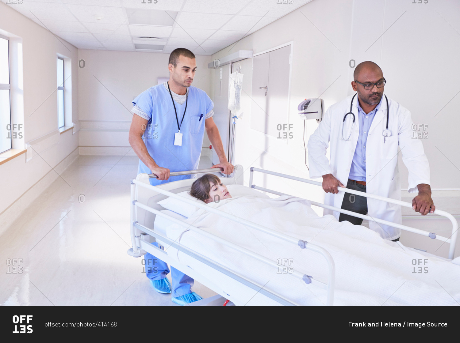 Doctors pushing patient in hospital bed through corridor
