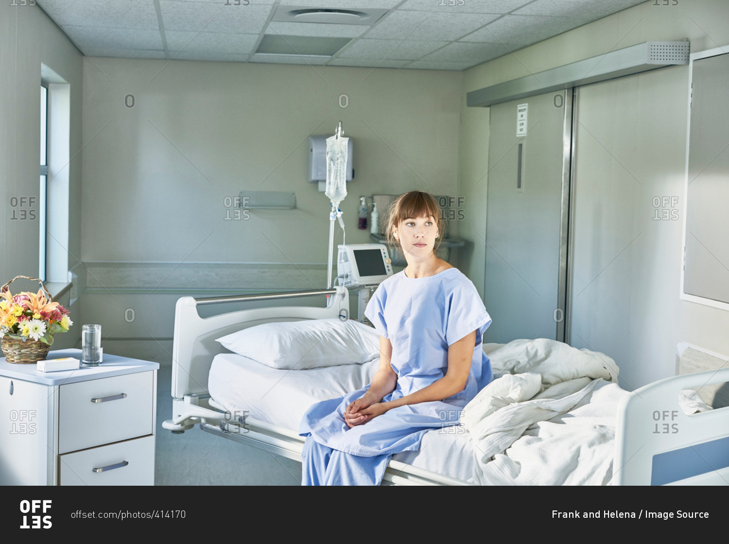 Patient sitting on hospital bed wearing hospital gown stock photo OFFSET