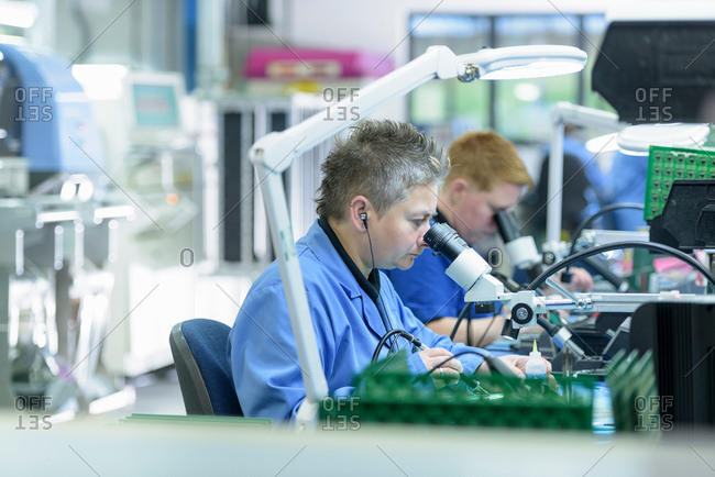 Female worker soldering component onto circuit boards in circuit board assembly factory