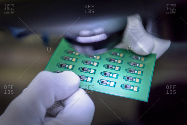 Worker inspecting circuit boards under microscope in circuit board assembly factory, close up
