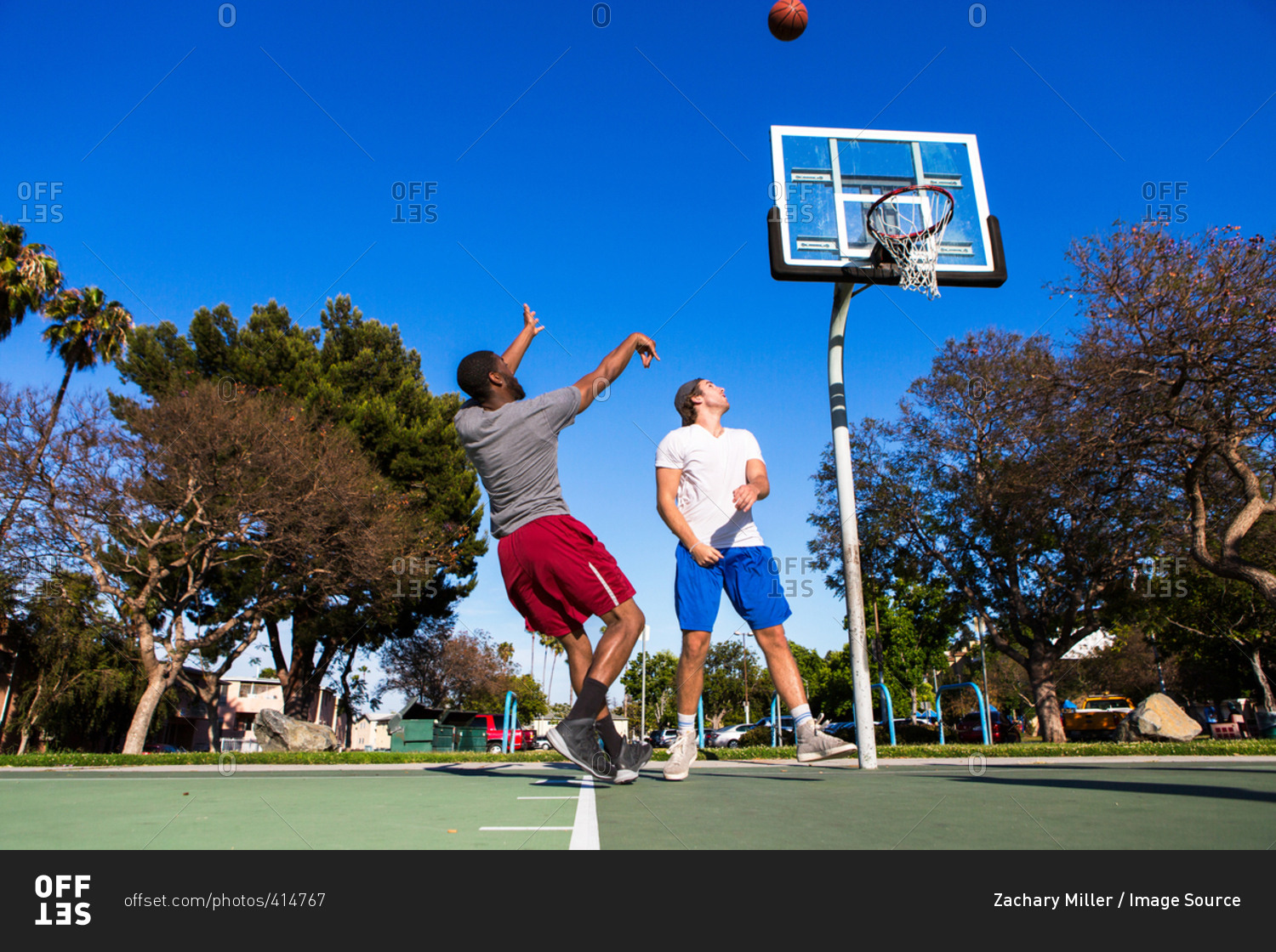 Young man throwing basketball towards basketball net on outdoor court